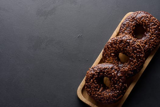 Chocolate donuts sprinkled with crushed nuts on a black table