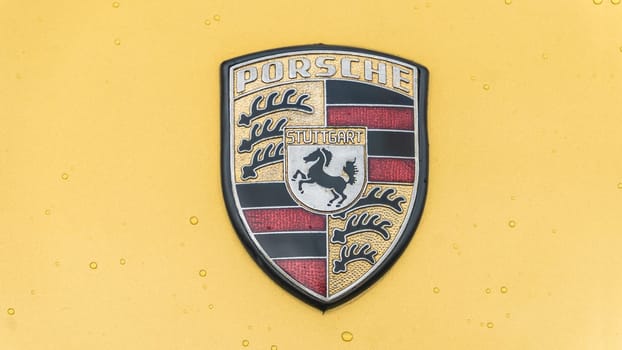 WETTENBERG, HESSE, GERMANY - 07 - 28 - 2023: Porsche Logo in detail with raindrops on a car show.