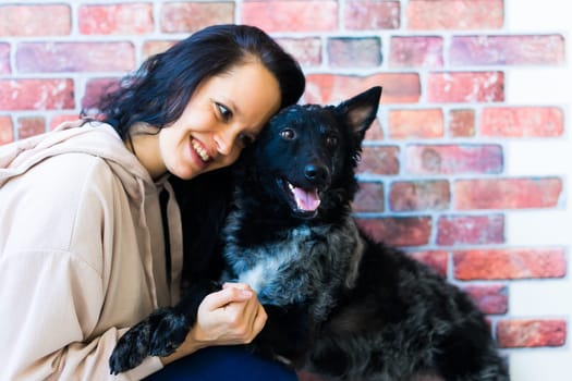 Happy brunette lady in a casual wear hugging mudi pet dog, studio background.