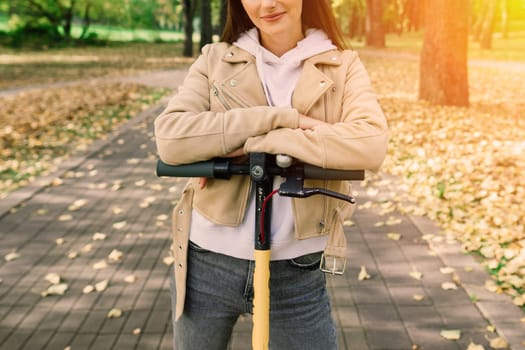 Young beautiful stylish woman riding electric scooter in autumn park, ecological transport