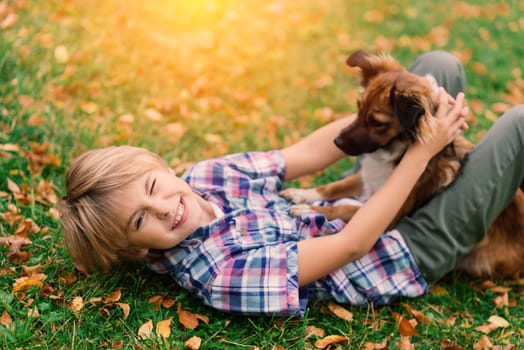 Boy hugging a dog and plyaing with in the fall, city park