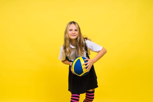 A teenager girl holds volleyball ball in hand and smiles on red yellow background. Studio photo.