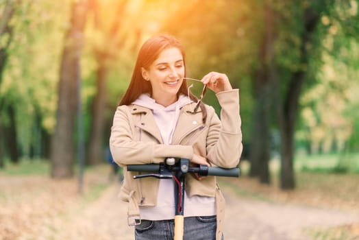 Young woman riding an electric scooter in autumn park. Green transport, traffic jam problems.