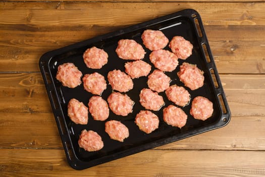 Top view of raw meatballs of minced meat on a baking tray on kitchen table