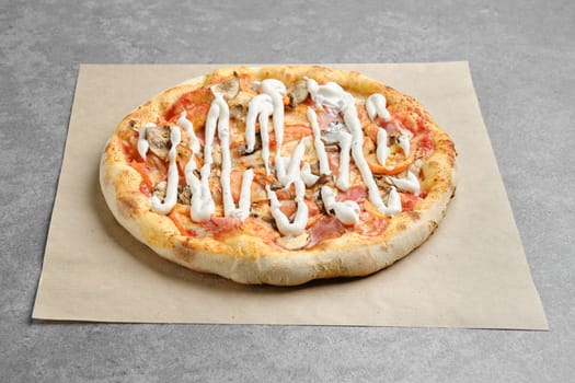 Pizza with ham, champignon and tomato slices covered with mayonnaise on parchment paper