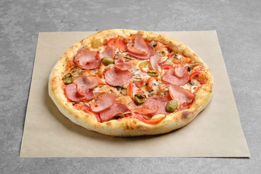 Pizza with ham, sausage, olives and bell pepper on parchment paper