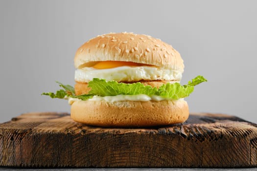 Chicken burger with fried egg and fresh iceberg lettuce salad on wooden board, front view