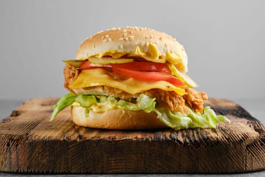 Chicken cheeseburger with fresh and pickled vegetables on wooden background, front view
