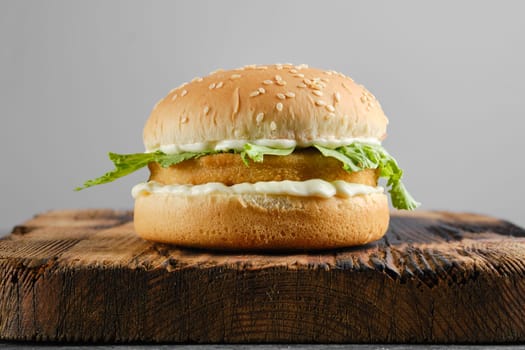 Chicken burger with fresh iceberg lettuce salad on wooden board, front view