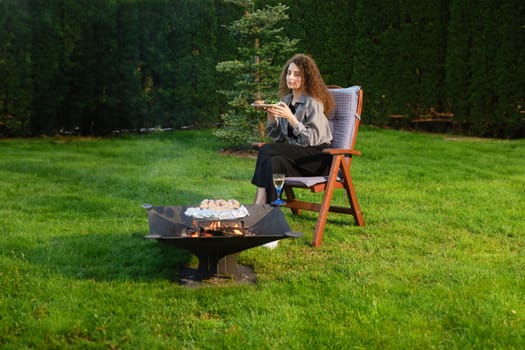 Young woman having late picnic at backyard near barbecue