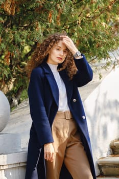 Pretty young woman touching long curly hair outdoors