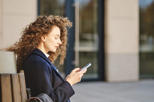 Young woman sits on bench and scrolling through social network feed