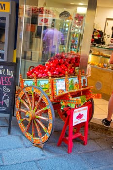 Sicily, Taormina, Italy - 28 September 2023. A brightly painted wooden cart with a basket of fresh pomegranates in front of a traditional fresh fruit juice shop in Taormina.