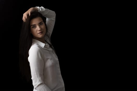 Smiling brunette girl is posing in studio on black background.  Horizontally.