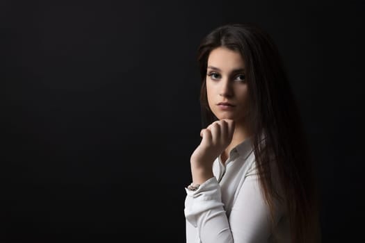 Portrait of beautiful  pensive long haired brunette girl  posing in studio on black background.  Horizontally.