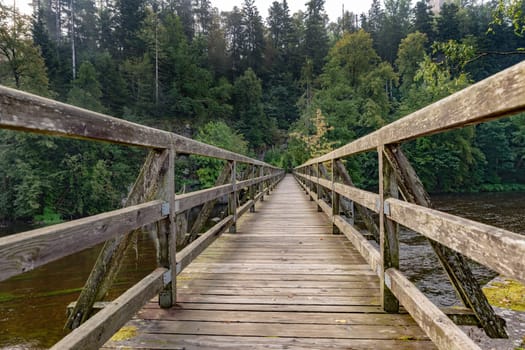 Bridge made of wooden boards over a green field with trees and wooded hills