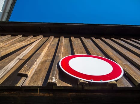Extreme bottom view of the no-passing traffic sign on a wood-paneled driveway in Bavaria against a blue sky.