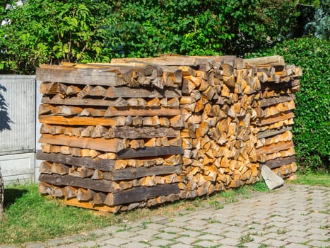 Compactly stacked logs in front of a green garden hedge in summer in Bavaria.