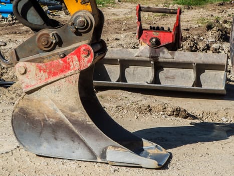 Close-up view of two excavator buckets at a construction site with a trench bucket in the foreground.