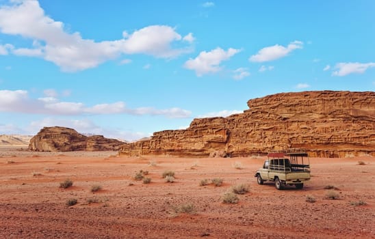 Dusty desert with rocky massif and blue sky above, off road desert vehicle in foreground. Typical scenery in Wadi Rum, Jordan.