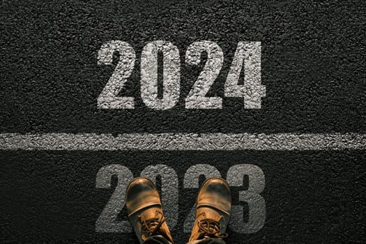 Man walks on asphalt and crosses the line by 2024. New year 2024. Men's legs with leather shoes go to 2024. End of 2023 and beginning of 2024