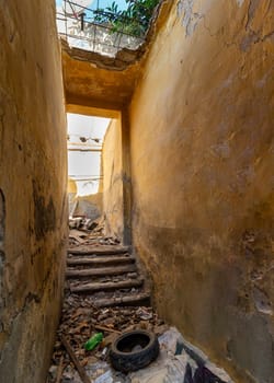Narrow passage with collapsed ceiling and collapsed staircase in ruins of an old abandoned building with ruined tyre in the floor