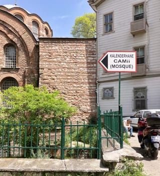Signpost pointing to the Eski Imaret Mosque, a historic mosque in Istanbul, Turkey, with part of the mosques facade in the background