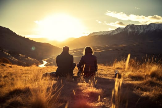 Couple sitting at campfire in evening during mountain trip. Couple having fun sitting at bonfire admiring mountain landscape. People relaxing at fire in the evening. Weekend trip. Travel to the mountains. Beauty in nature