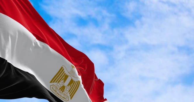 National flag of Egypt waving in the wind on a clear day. Horizontal red, white and black bands. Egyptian eagle emblem centered in white band. 3d illustration render. Fluttering fabric