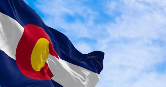 Close-up of Colorado state flag waving in the wind on a clear day. Three blue, white, and blue stripes. Red C with gold disk on top. 3D illustration render. Fluttering fabric