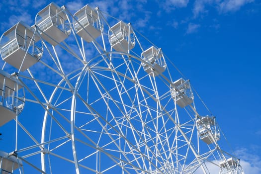 Ferris wheel in the park. White ferris wheel against the blue sky.