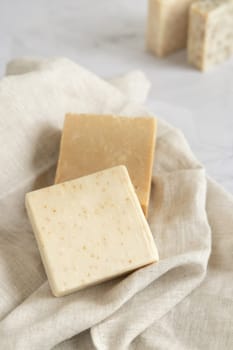 Beige handmade soap bars on cream linen towel close up. Natural herbal soaps for face and body care. Using organic skincare products in everyday bath routine