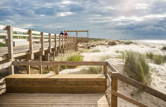 Visitors couple walking over wooden footbridge of Monte Gordo beach, Vila Real de Santo Antonio, Portugal