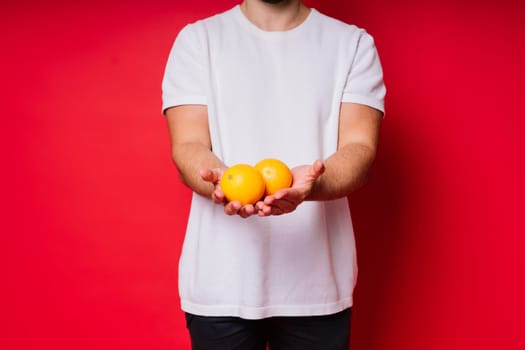 Studio portrait of a handsome young man posing with an orange against red background.