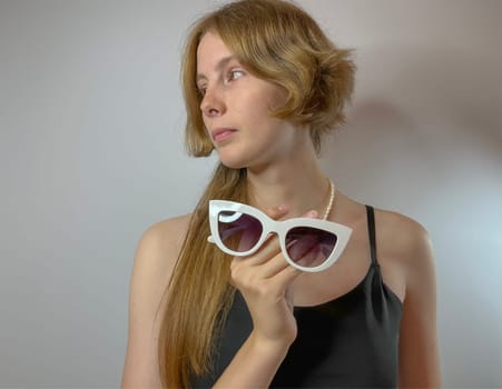 a young girl holds a pair of white-framed sunglasses in her hands