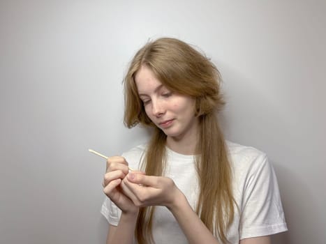 on a light background, a young blonde gives herself a manicure
