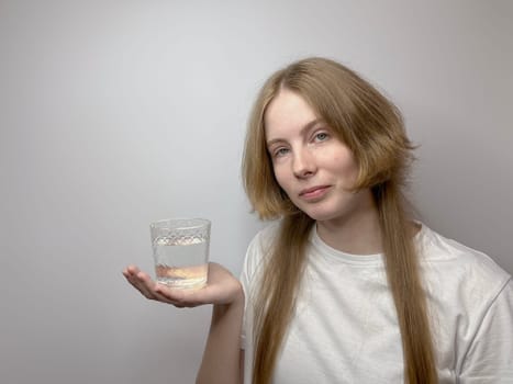 on a light background, a young girl holds a glass of water in the palm of her hand