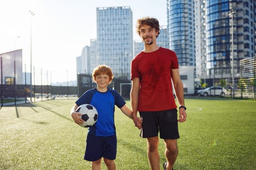 Happy father and son child walking on football field after successful game. Family sport recreation activity