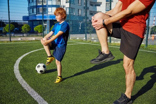Sportive dad and son doing physical workout and warming legs up before football game training at city stadium
