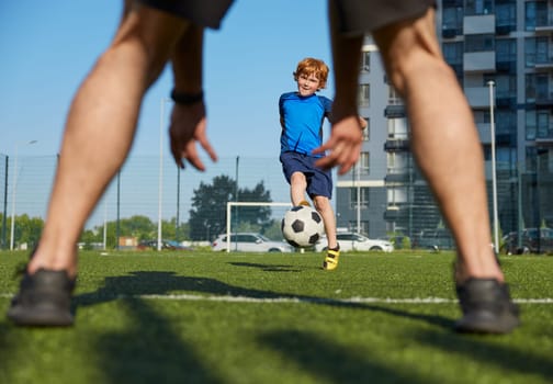 Father and son playing family football summer camp for training at city stadium. Closeup shot of daddy catching ball while boy child kicking