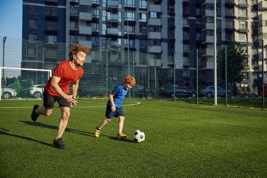 Dad and son child playing soccer on field. Friendly confrontation of parent and kid. Happy family playful time together