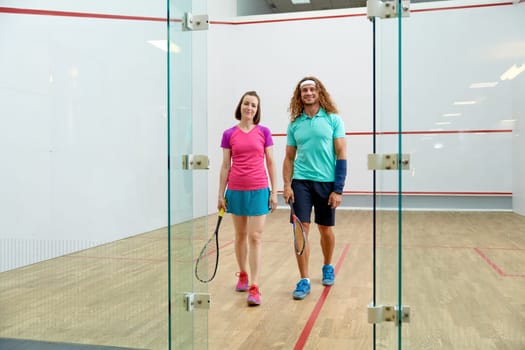 Satisfied man and woman athlete after successful squash game. View from glass sportive club doorway