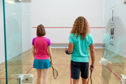 Man and woman squash player holding racket view from back standing in doorway of indoor sport court. Concept of healthy and active lifestyle