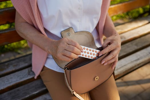 Crop shot of old woman taking pills from bag after feeling bad on walk in park. Elderly people health problem concept