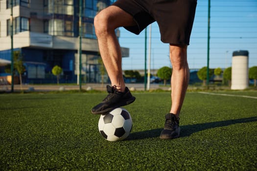 Crop view if man holding foot on soccer ball standing over football field. Training favorite game outdoor