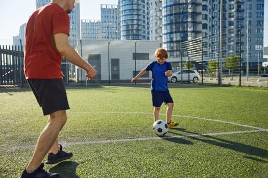 Father and son playing soccer training on football pitch during sunny summer day. Family weekend sports activity