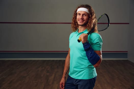 Portrait of male squash player standing with racket ready for game looking confidently at camera