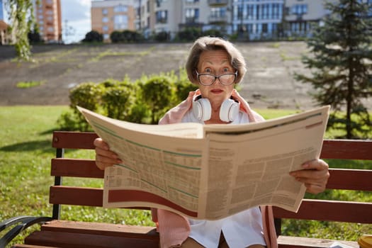 Surprised or shocked elderly woman reading daily newspaper finding overwhelmed news in morning in public park