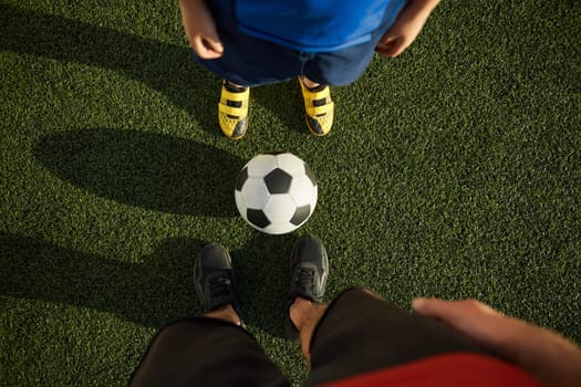 Father and son child playing football on outdoor field. Focus on feet of adult and young soccer players