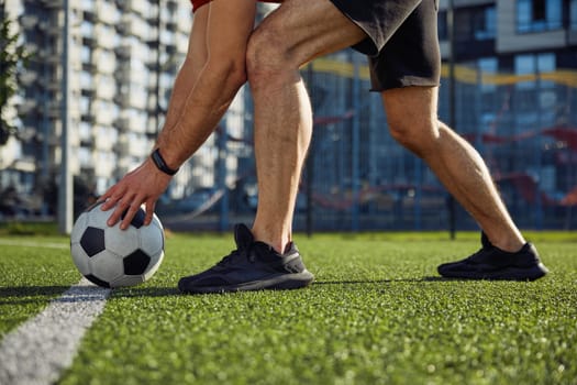 Start football match. Male player putting ball on strip line on center of soccer field cropped closeup shot